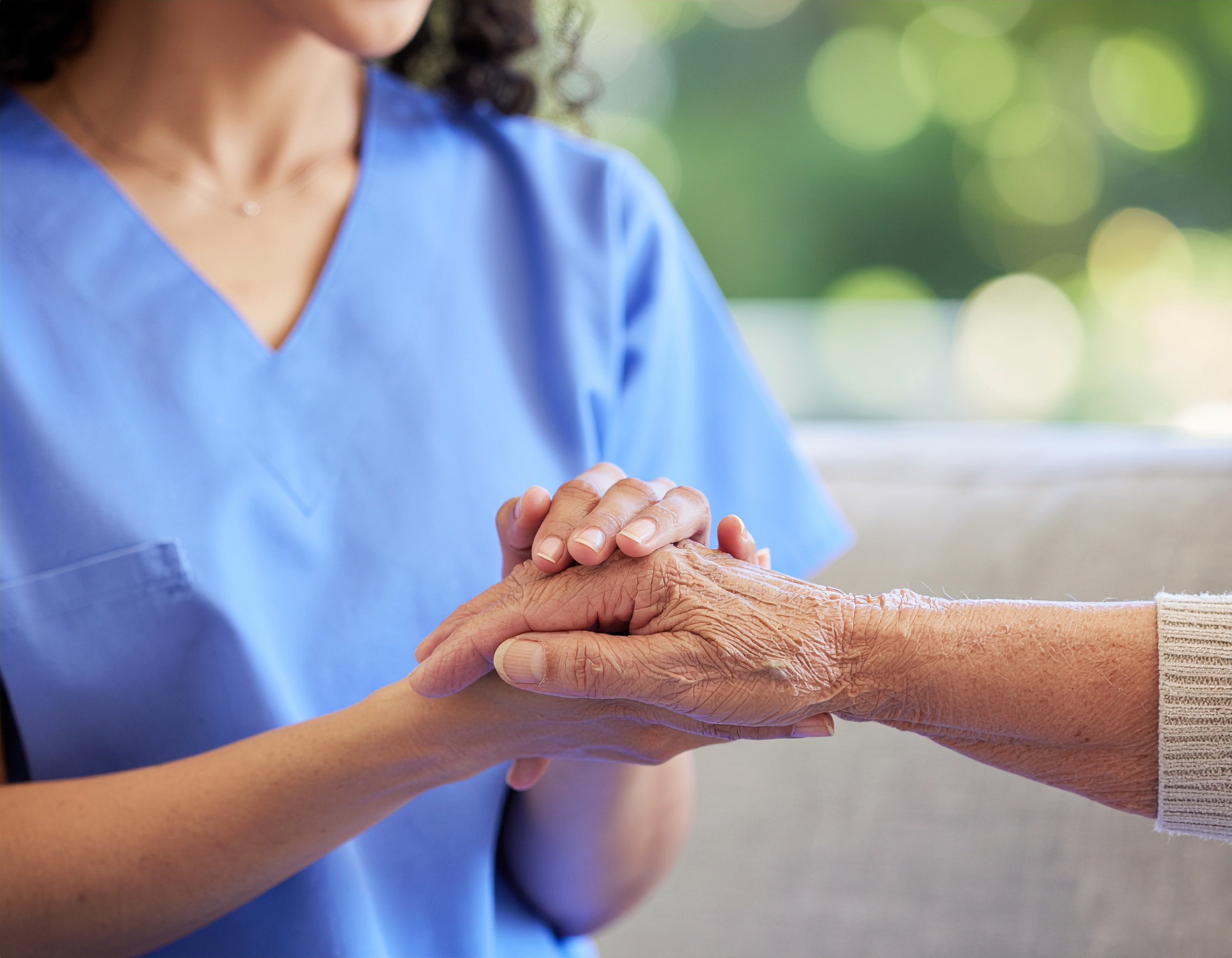 Caregiver gently holding an older adult's hand in a bright, calm setting